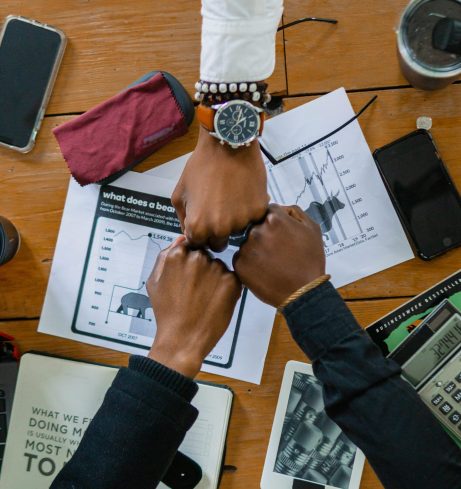 Coworkers joining fists over office desk, symbolizing teamwork and motivation.